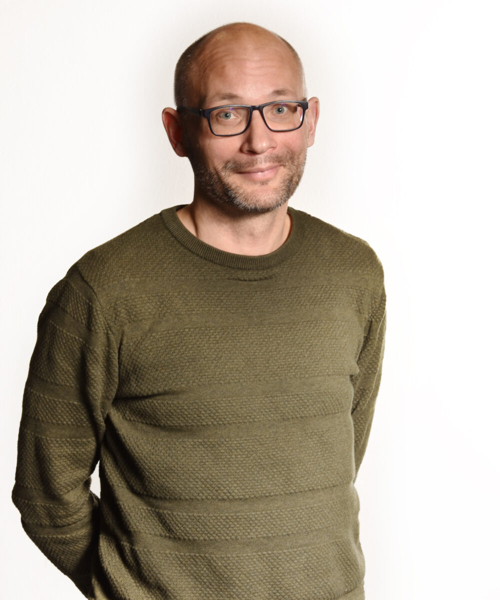Collega Intermax kale man met bril, legergroene trui en handen op zijn rug